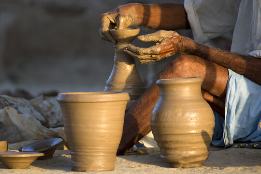 View of a potter shaping a clay vessel on a wheel with finished pots in the foreground in Multan City, Punjab, Pakistan.
