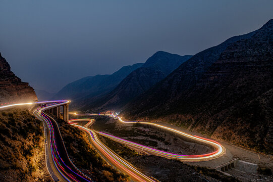 View of the winding Fort Munro Road at night with vibrant light trails from vehicles navigating the mountainous terrain in Fort Monroe, Punjab, Pakistan.