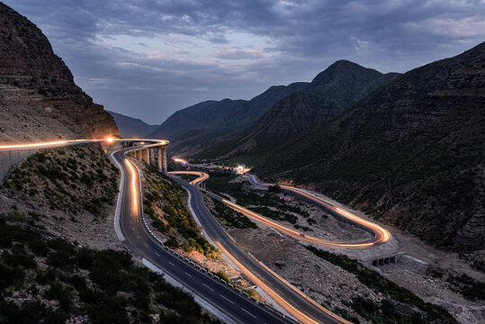 View of Fort Munro Road winding through the rugged mountains of the Sulaiman Range with light trails from vehicles at dusk in Fort Monroe, Punjab, Pakistan.
