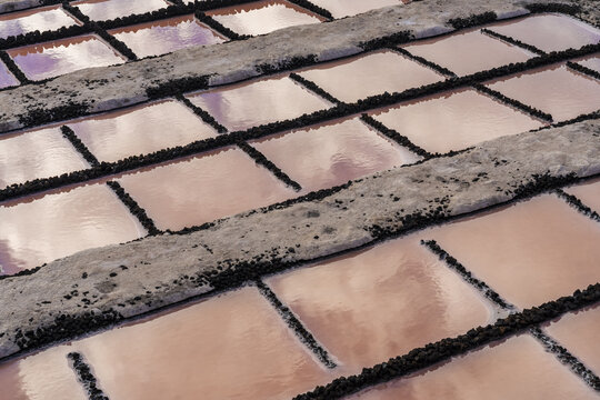 View of Salinas de Fuencaliente with pink salt pans, volcanic rock borders, and sky reflections in Santa Cruz de La Palma, Canarias, Spain.