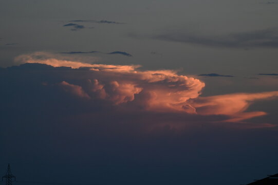 View of dramatic sunset clouds with pink and orange hues illuminated by the setting sun against a dark sky, with a power pylon silhouette in Jahanian, Punjab, Pakistan.