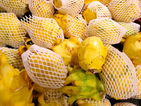 Vibrant yellow dragon fruits wrapped in protective white foam netting, displayed in a dense pile.