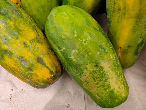 A top-down close-up of whole green Bangkok papayas with yellow patches, showcasing textured skin and natural fresh produce details.