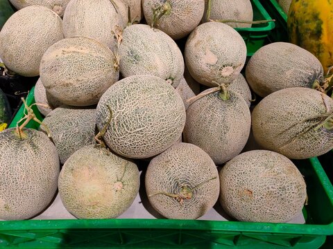 A wide shot of whole red sweet melons piled high in green display crates, highlighting their round shapes and netted skins.
