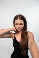 Naklejka premium Young woman taking selfie with serious expression, long brown hair, wearing black top, looking at camera