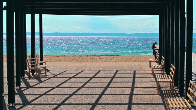 Empty wooden benches overlooking tranquil sparkling blue sea with distant horizon and clear sky.