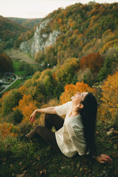Cheerful young woman laughing while sitting on a cliff overlooking a beautiful autumn valley in Ojcow National Park, Poland.