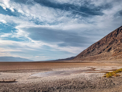 View of Death Valley with salt flats, rugged mountains, and a dramatic cloudy sky in Inyo County, California, United States.