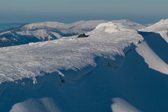 View of a small tent pitched on the snow-covered summit of Dumbier mountain in the Low Tatras, with winter peaks in the background under a clear sky in Nizke Tatry, Zilina Region, Slovakia.