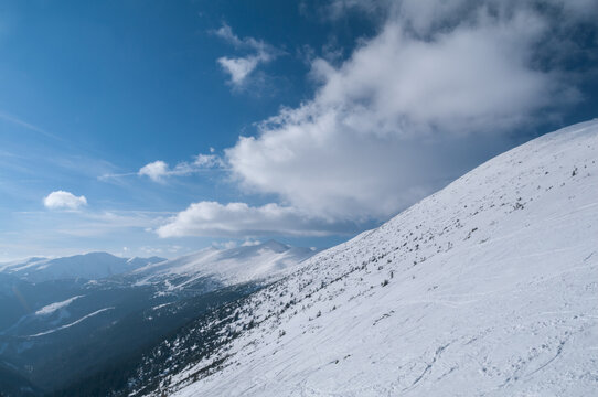 View of the snow-covered slopes of Dumbier mountain under a bright blue sky with scattered clouds in Nizke Tatry, Zilina Region, Slovakia.