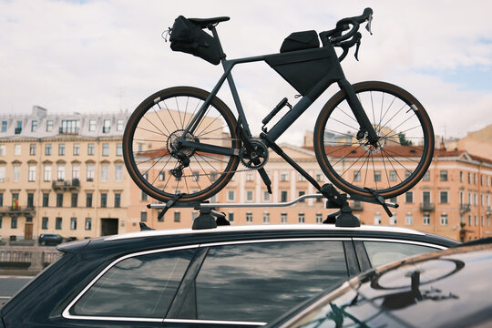 Touring bicycle with travel bags secured to a roof rack on a passenger car in an urban setting, illustrating cycling travel, active lifestyle and outdoor recreation.