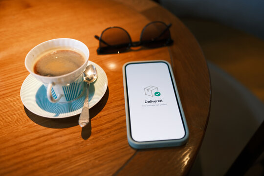 Smartphone displaying a successful package delivery notification beside coffee and eyeglasses on a table, illustrating e-commerce logistics and convenient digital services.