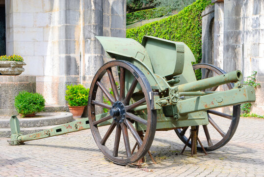 Historic artillery cannon displayed at Il Vittoriale degli Italiani in Gardone Riviera, Italy, surrounded by stone architecture, greenery and Mediterranean gardens.