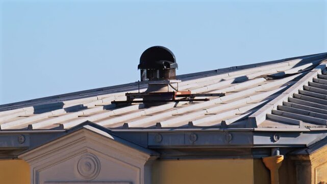 Close-up of metal roof vent spinning against clear blue sky on sunny day, urban scene detail.