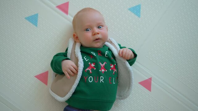 Three month old baby boy in christmas outfit looking at camera.