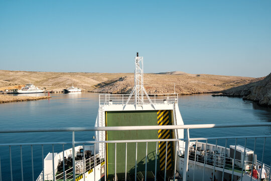 View of the Misnjak Ferry Port with a ferry boat approaching the dock, calm blue waters, and rocky coastal landscape, Barbat na Rabu, Primorsko-goranska zupanija, Croatia.