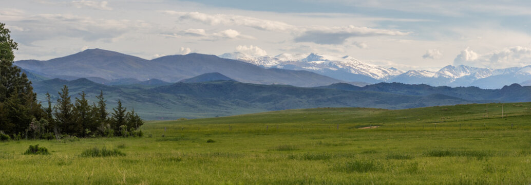 View of the Rocky Mountains panorama with snow-capped peaks rising above lush green fields and evergreen trees in Fort Collins, Colorado, United States.