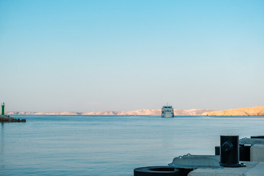 View of the ferry Stinica - Misnjak sailing on the calm sea towards the rocky coastline under a clear blue sky in Stinica, Croatia.