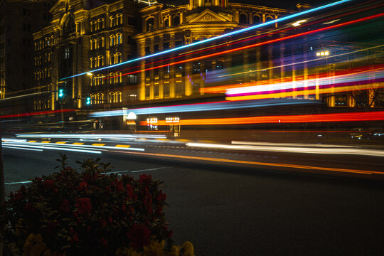 View of The Bund at night with long exposure light trails from passing traffic, illuminated historic architecture, and foreground flowers in Shanghai, Shanghai, China.