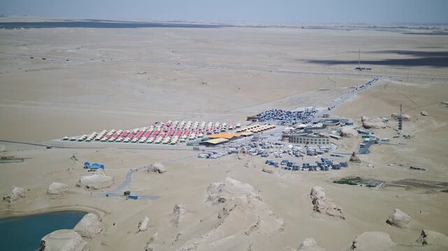 High-Angle Aerial View of RV Campsite and Resort Hotel in Wusute Water Yadan Scenic Area: Luxury Camping Tents, Wind-Eroded Yadan Landform, Blue Lake and Qaidam Gobi Desert