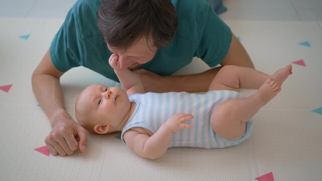 Baby boy touching father's face on soft floor mat.