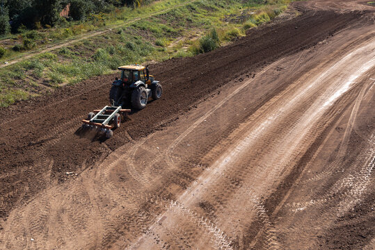 Aerial view of a tractor leveling soil with a disc harrow on a construction site