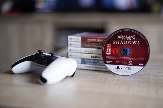 BRECHT, BELGIUM &ndash; August 28, 2026: Closeup portrait of a stack of a PS5 controller, playstation games with a game disc standing against it, highlighting physical gaming media.