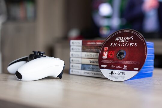 BRECHT, BELGIUM &ndash; August 28, 2026: Closeup portrait of a stack of PS5 playstation games with a game disc standing against it and a controller lying next to it, highlighting physical gaming media.