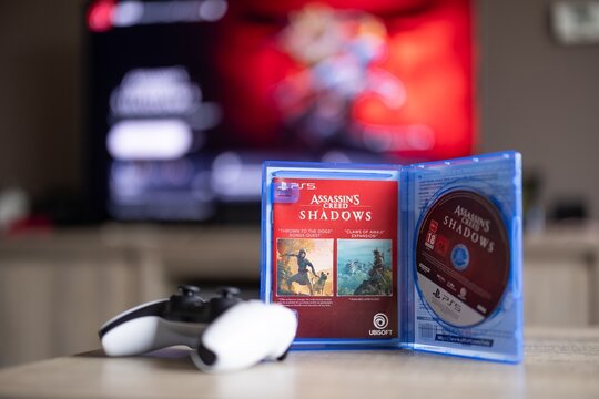 BRECHT, BELGIUM &ndash; August 28, 2026: Portrait of a PS5 game case standing open with a physical game disc in it and a controller lying next to it with the playstation home screen in the background.