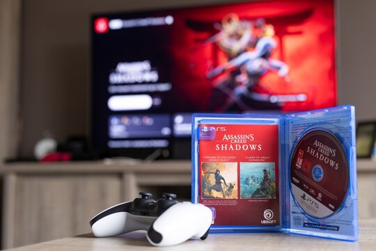 BRECHT, BELGIUM &ndash; August 28, 2026: Closeup portrait of a PS5 game case standing open with a physical game disc in it and a controller lying next to it with the playstation home screen in the back.