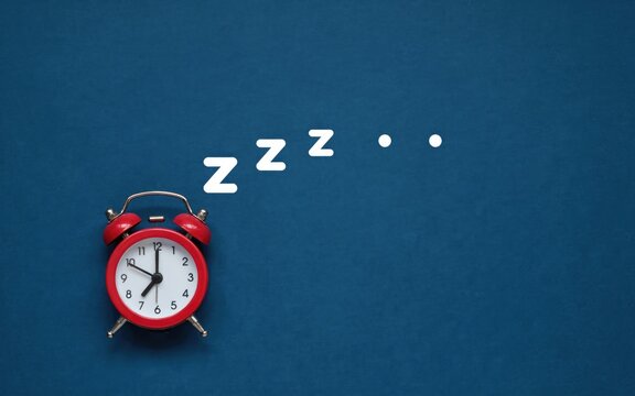 Red twin-bell alarm clock with white zzz sleep symbols on blue background