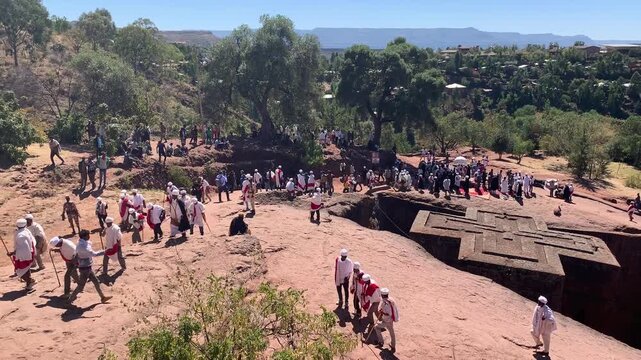 Ethiopia - 26 August 2026: View of the rock-hewn Church of Saint George in Lalibela with pilgrims in traditional white clothing gathered for a religious ceremony under a bright sky.