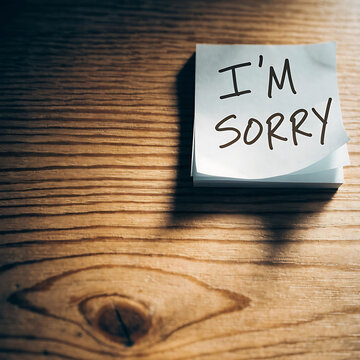 A handwritten note with the text I am sorry placed on a wooden desk