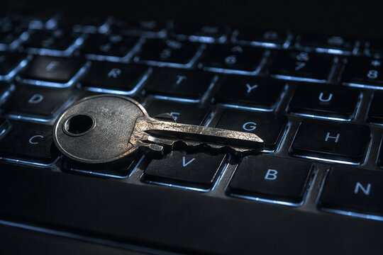 Silver metal key resting on illuminated computer keyboard for cyber security