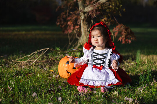 Toddler in Red Hooded Halloween Costume With Pumpkin Bucket