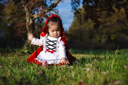 Toddler in Red Hooded Costume Sitting on Grass for Halloween
