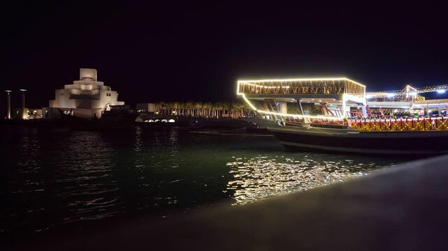 Doha, Qatar - 21 August 2026: View of the illuminated Museum of Islamic Art and traditional dhow boats docked at the waterfront at night.