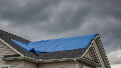 Fototapeta premium Blue tarp covering damaged asphalt shingle roof under stormy sky
