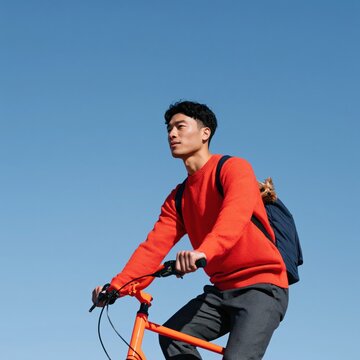 Young man riding orange bicycle with small dog and backpack for urban commuting lifestyle background and outdoor banner design