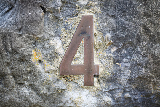 House number four sign in aged metal, mounted on a rugged rock wall, displaying a single weathered numeral with rustic tarnished metallic surface finish