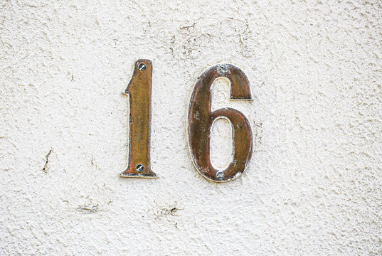 House number 16 sign in rusted metal digits, fixed on a rough painted wall, displaying one and six numerals with weathered vintage metallic patina texture