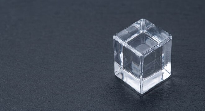 Single crystal clear craft ice cube on dark stone surface