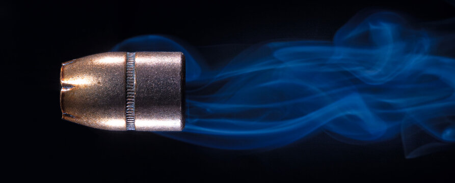 Hollow-point pistol bullet with copper plating on a black background with smoke behind