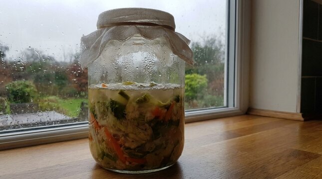 Clear glass jar filled with pickled vegetables and brine, suggesting homemade preservation and culinary art, perfect for food preparation and kitchen settings, rustic aesthetic elements
