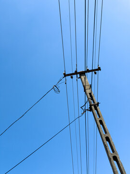 Power lines stretch across a clear sky. View of power lines on a tall pole against a clear blue sky during daytime. There are no clouds in sight.