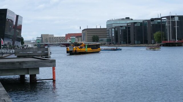 Copenhagen, Denmark - 15 August 2026: View of a yellow canal boat navigating the harbor with modern buildings and calm water in the background.
