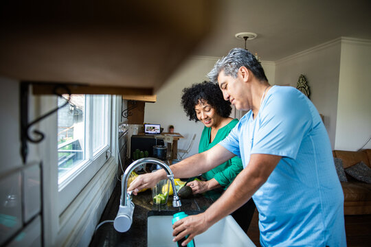 Smiling couple preparing healthy smoothie at home kitchen sink