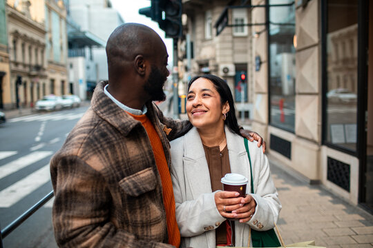 Smiling couple walking on city street with takeaway coffee