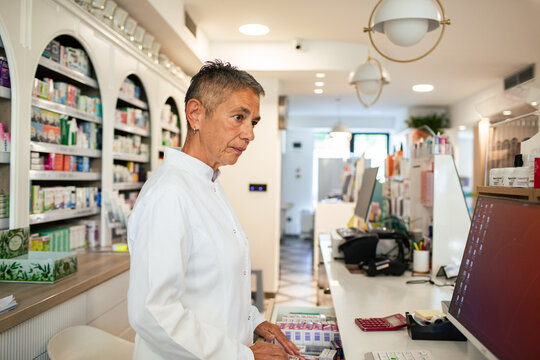Senior pharmacist organizing medicine at counter in modern pharmacy