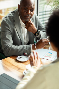 Mature businessman listening during cafe meeting with charts
